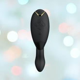 A sleek black Womanizer Duo 2 Rabbit Air Pulse Vibrator by Womanizer, resembling a mini remote with buttons on its surface, is set against a blurred backdrop of circular lights in pastel hues. It elegantly features Pleasure Air technology for enhanced clitoral stimulation.
